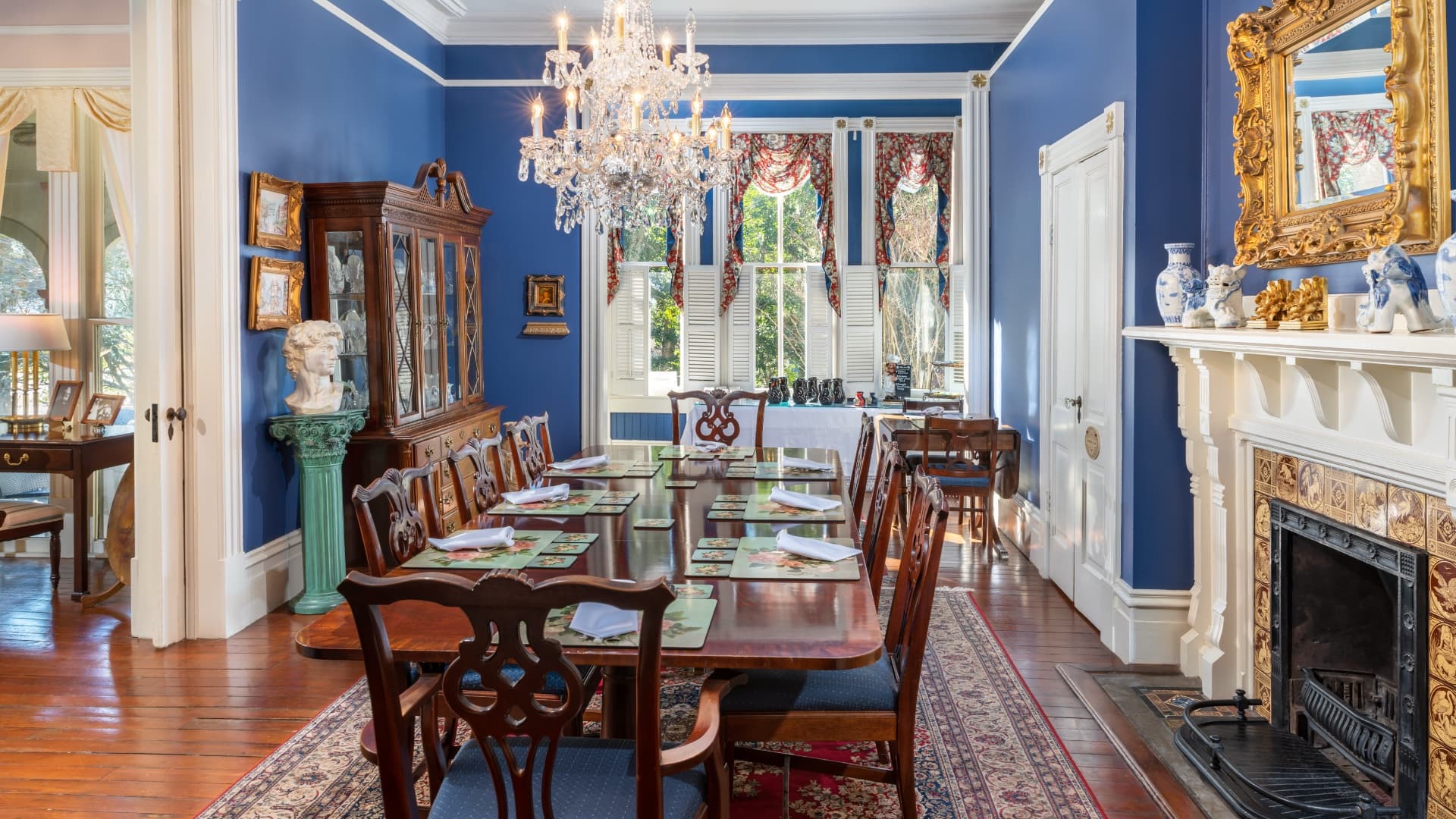 A formal dining room with a long wooden table, blue walls, a crystal chandelier, and elegant decor.